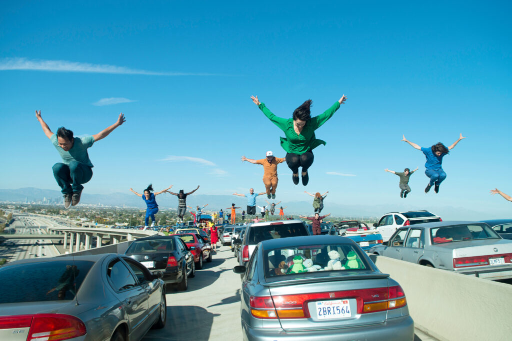 a large group of dancers jumping on top of cars parked on a highway ramp