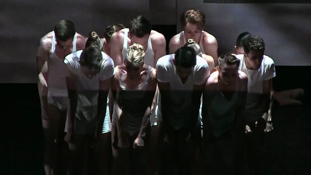 a group of dancers wearing white, huddled on stage and looking down