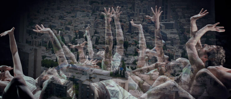 A group of dancers on the floor looking and reaching up with outstretched hands.