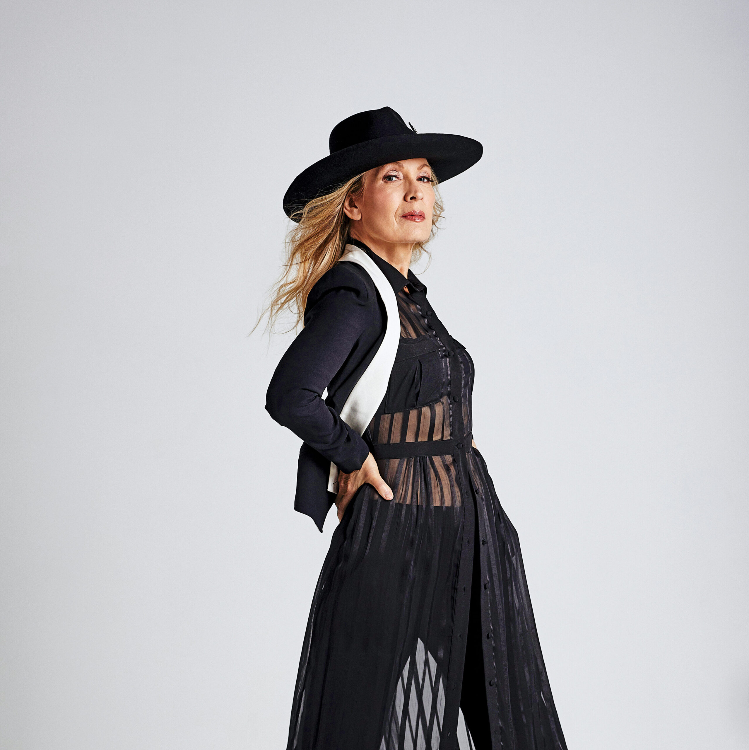 blonde woman wearing a black wide brimmed hat and a black striped mesh dress