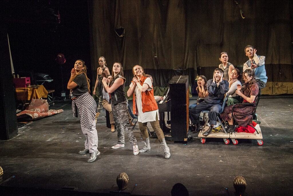 a large group of performers clasping their hands and looking towards the right corner