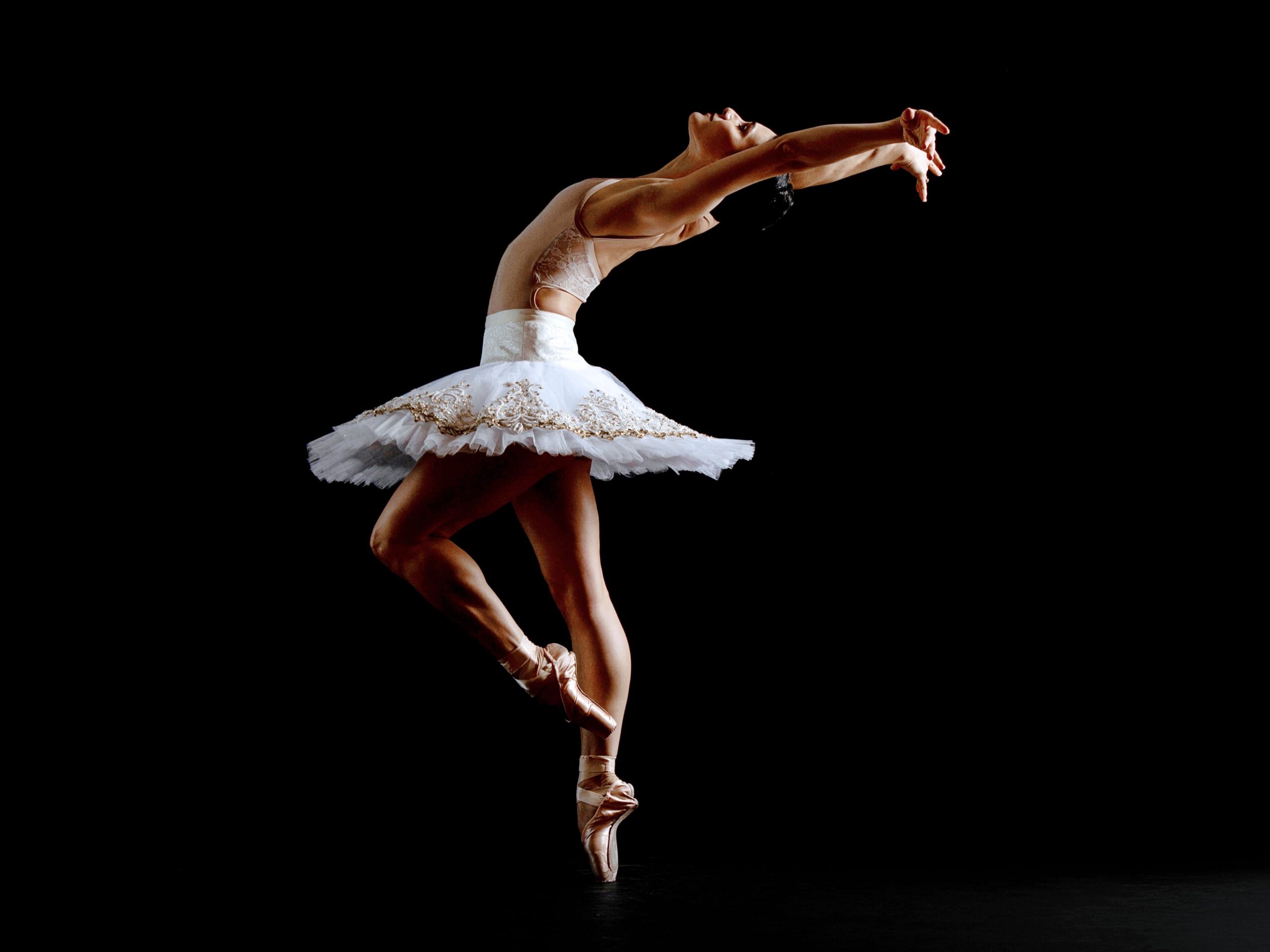 Female dancer wearing a white tutu dancing in front of black backdrop