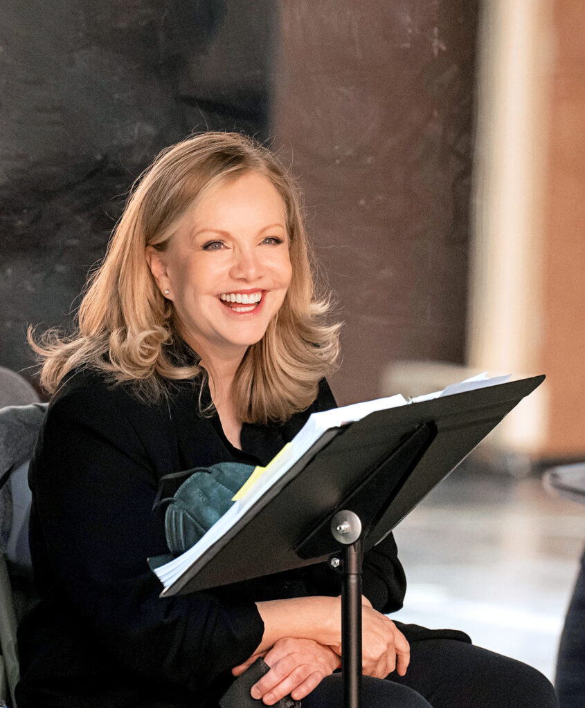 Susan Stroman laughs as she sits at the front of a studio, a music stand with an open score or script in front of her. Her blonde hair falls neatly to her shoulders; she wears all black.