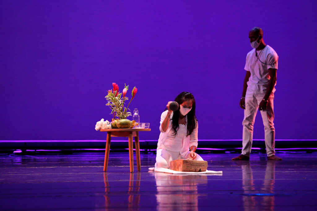two dancers on stage with a table, fruit, and flowers