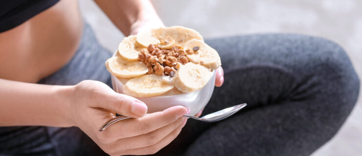 a woman holding a bowl of yogurt, bananas, and granola