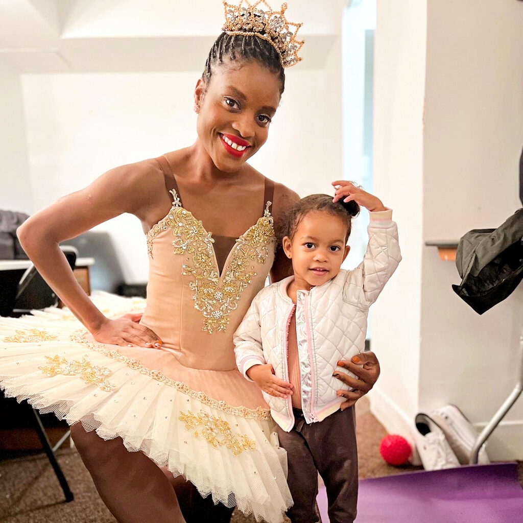 a dancer wearing a tiara and pink and white tutu hugging a small child smiling 