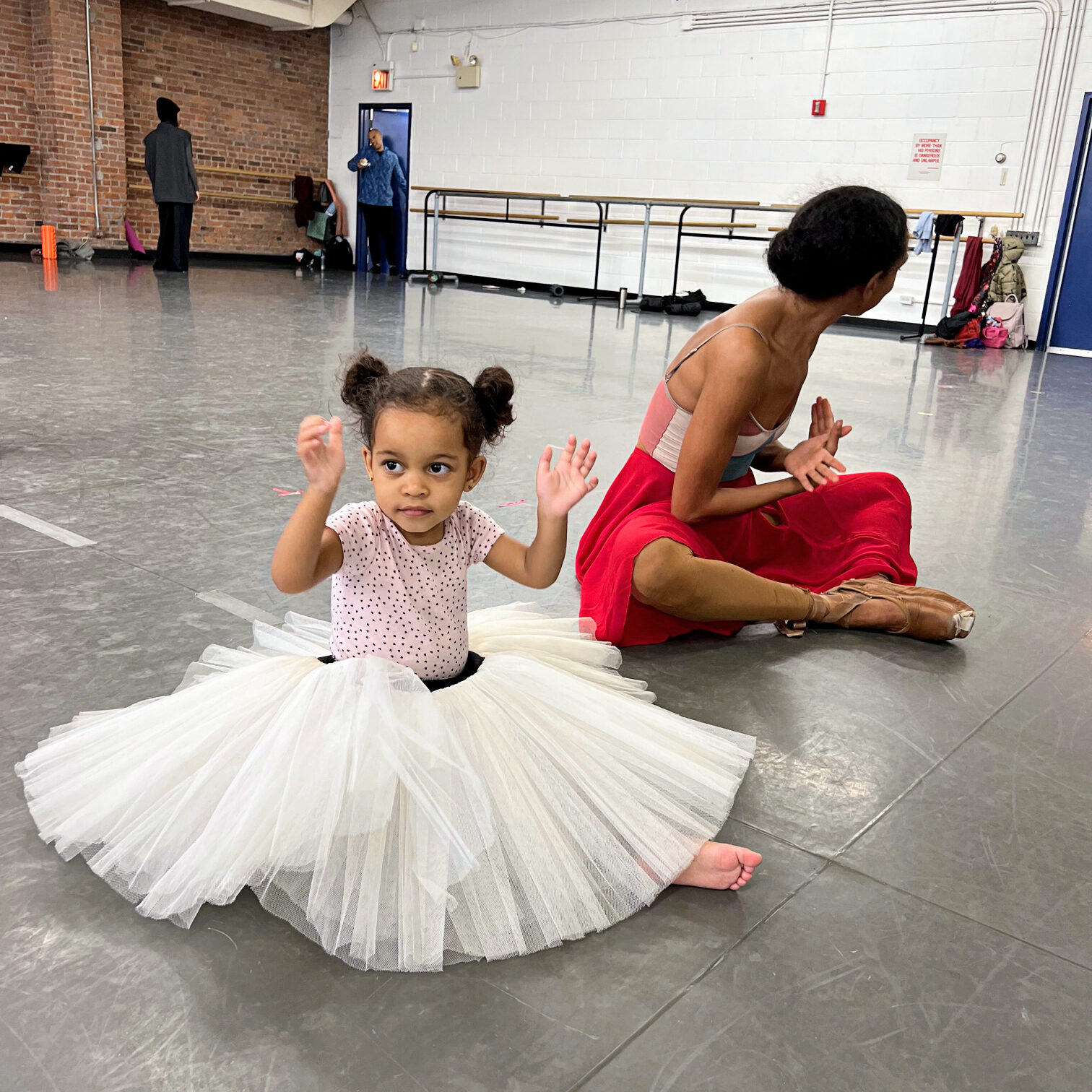 a little girl wearing a white pancake tutu sitting on the floor in the studio