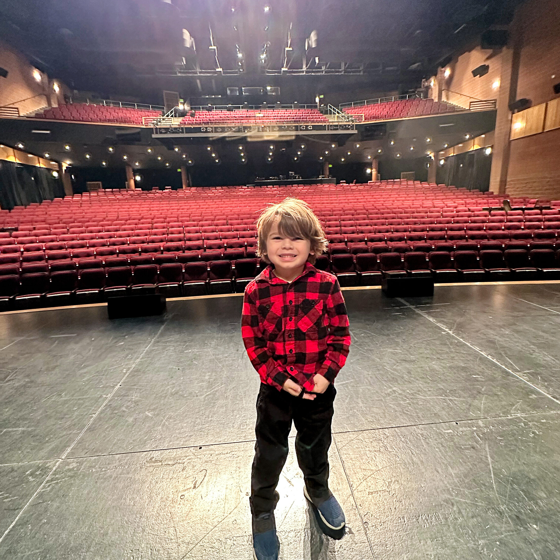 a young boy wearing red plaid standing on stage smiling 
