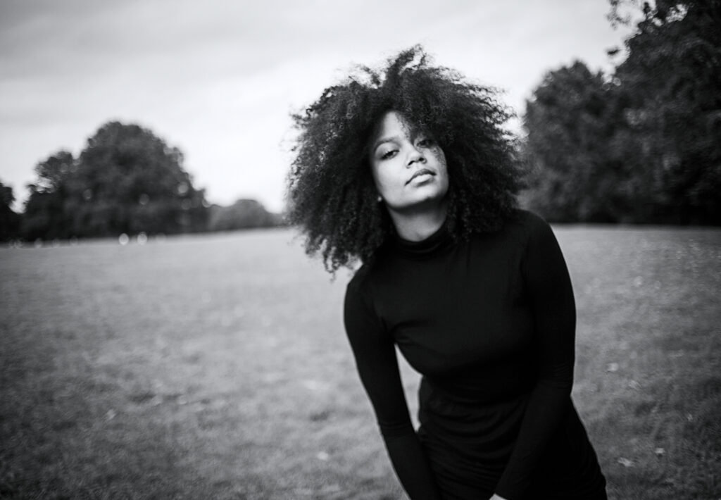 a female dancer with curly hair wearing a black turtle neck while standing in a field