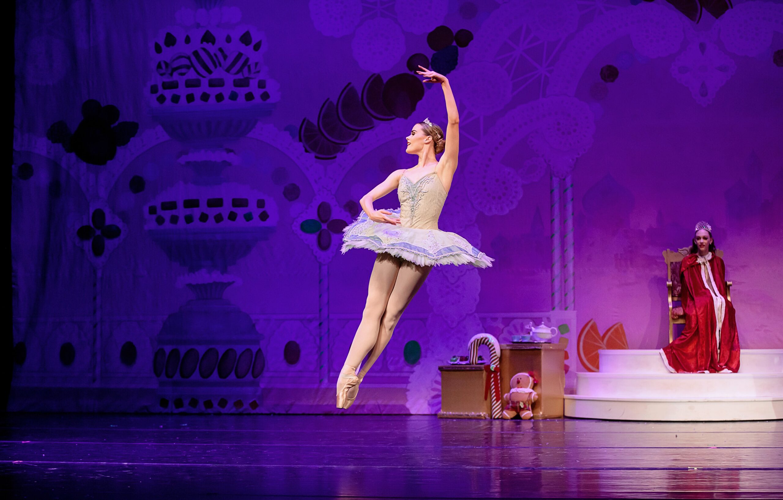 a female dancer wearing a purple tutu performing an assemble on stage.
