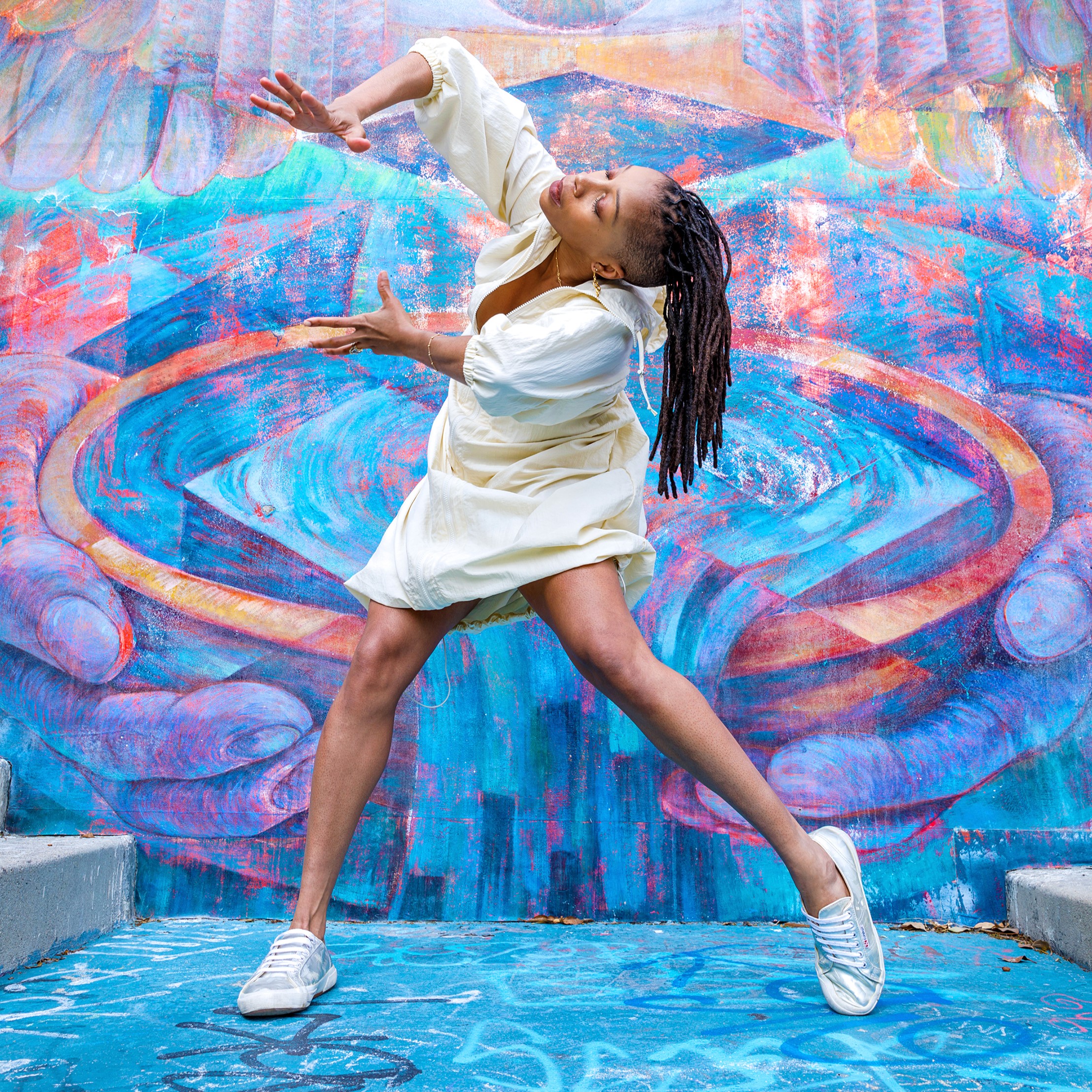 a female dancer wearing a white dress and sneakers dancing in front of a mural