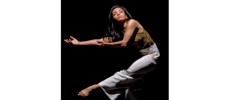 a female dancer against a dark backdrop reaching her arms and a leg towards the left