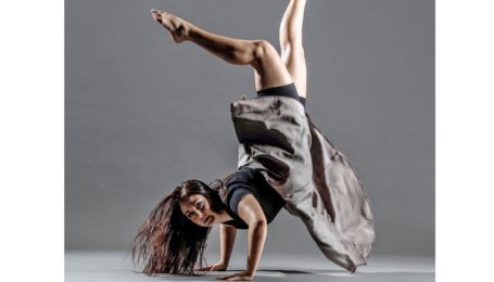 a female dancer wearing a grey skirt performing a handstand with her arms and legs slightly bent
