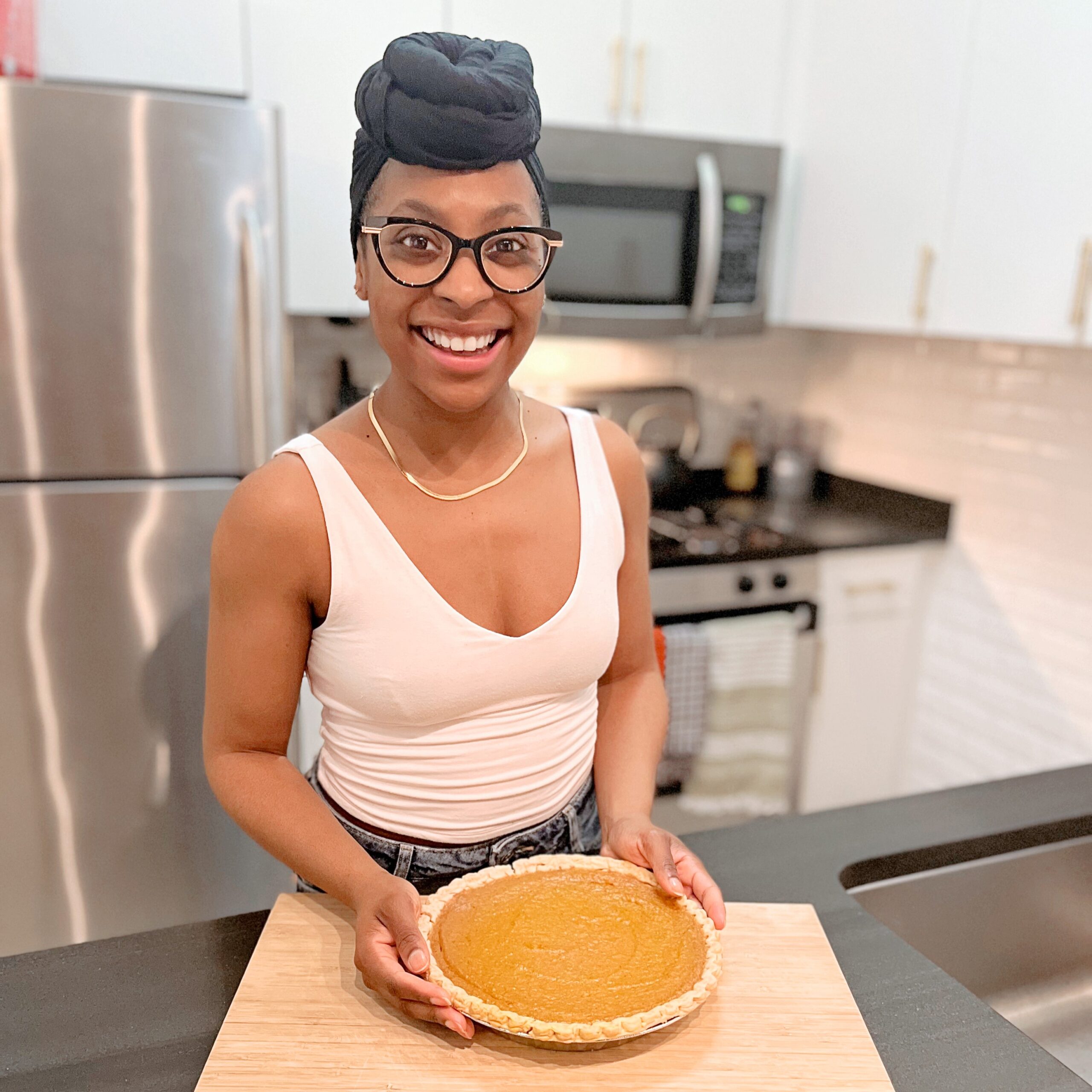 a woman wearing a pink tank top and glasses holding a pie in a kitchen