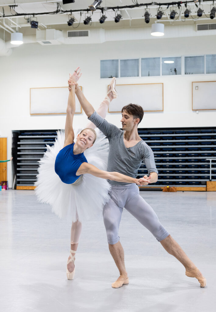 a male dancer holding a female dancer's hands as she leans forwards in a penche 