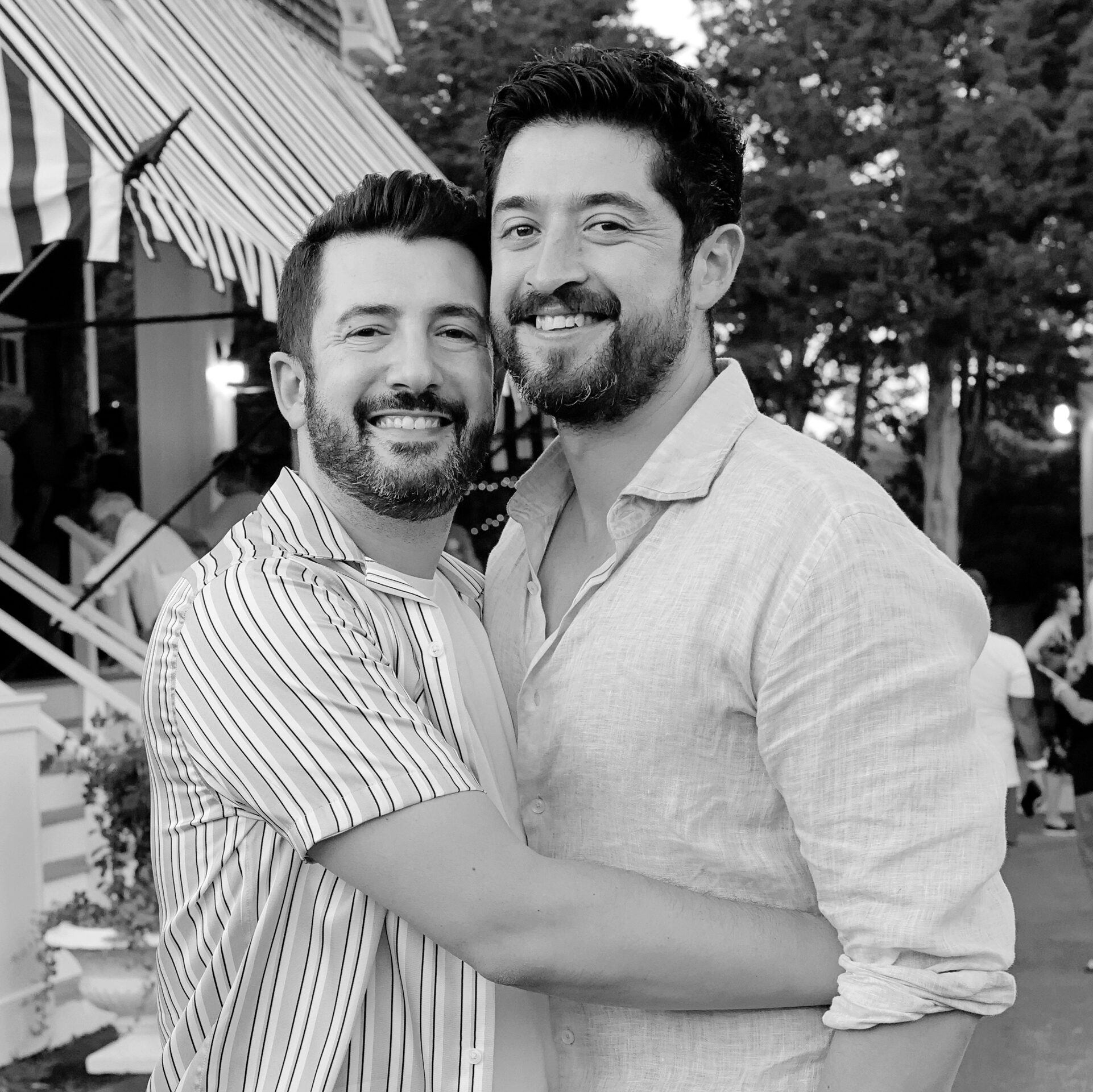 two males wearing button down shirts, hugging and smiling at the camera