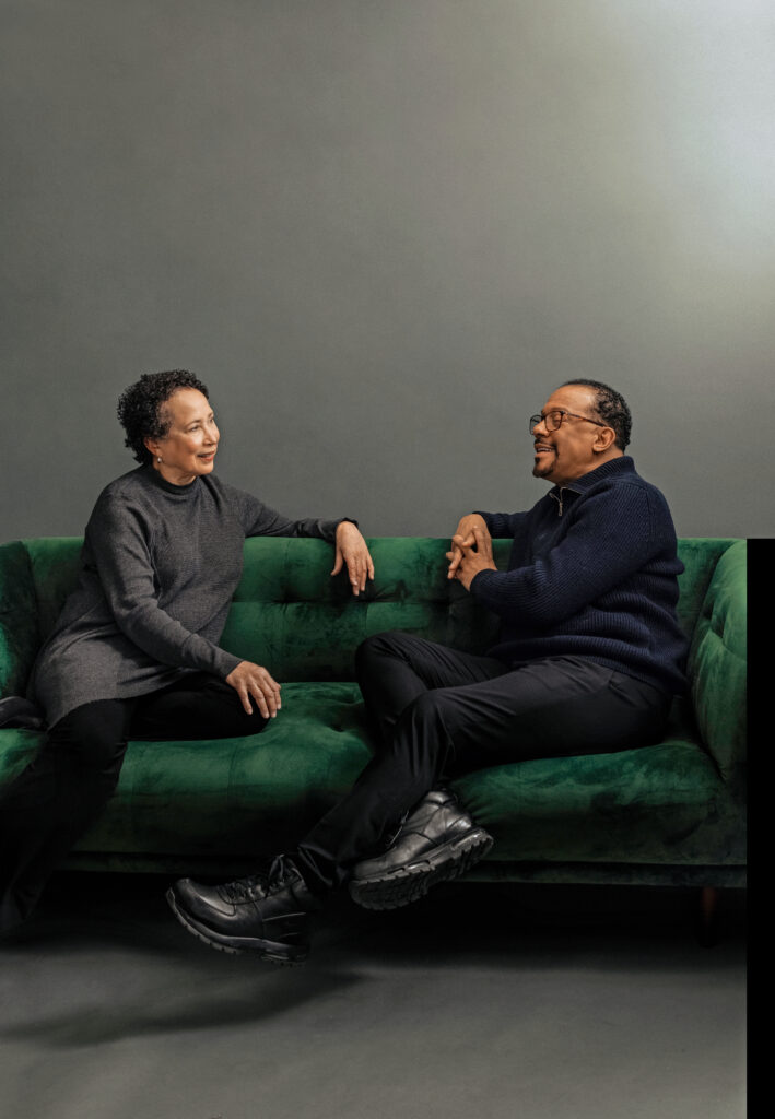 Virginia Johnson and Robert Garland are captured mid-conversation as they sit facing each other on a green velvet couch. Johnson smiles faintly as she Garland speaks.