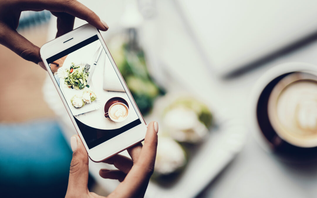 a hand holding a smartphone to take a photo of the food on the table