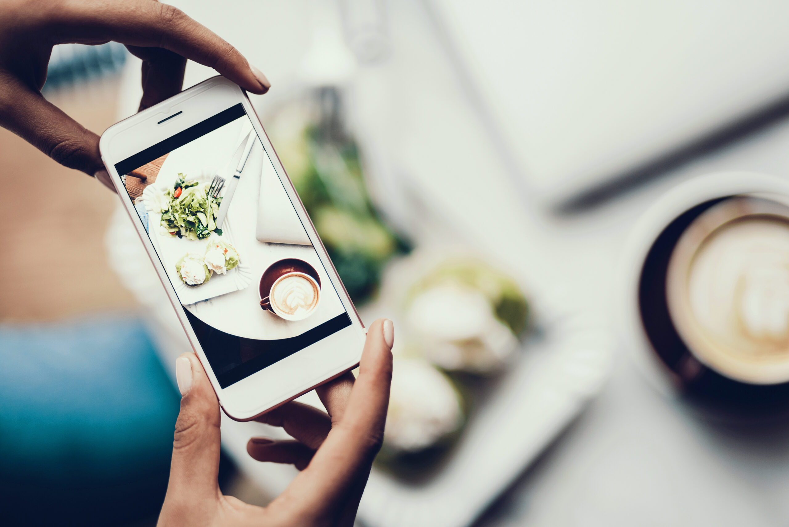 a hand holding a smartphone to take a photo of the food on the table
