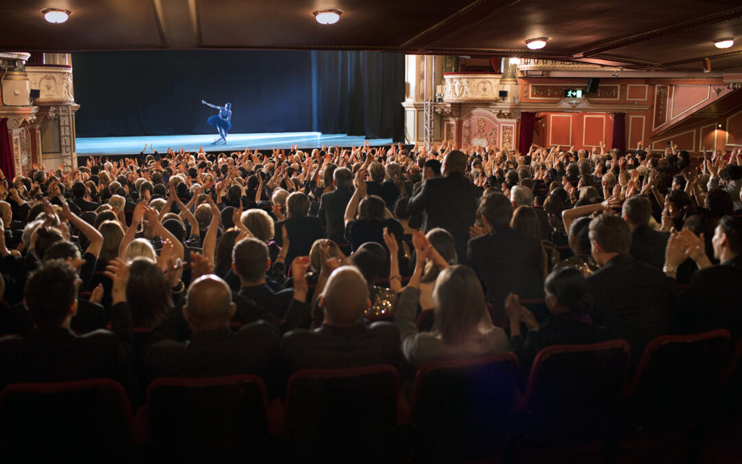 a large audience applauding for a ballerina on stage