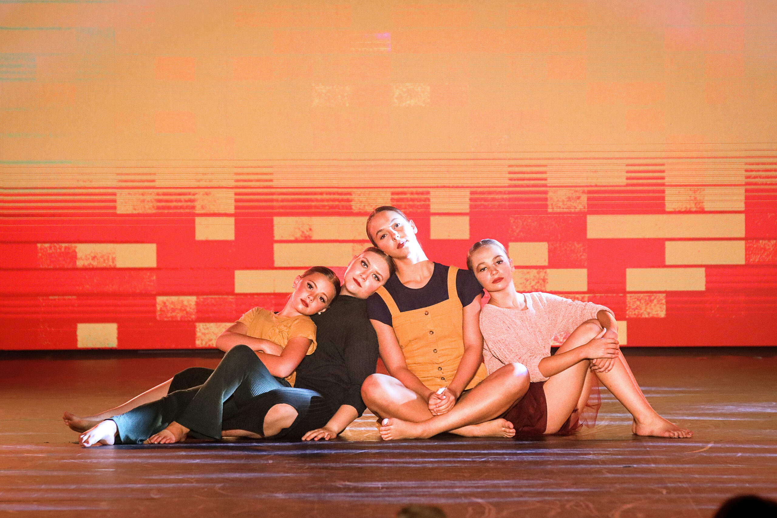 4 dancers sitting on the floor leaning against each other