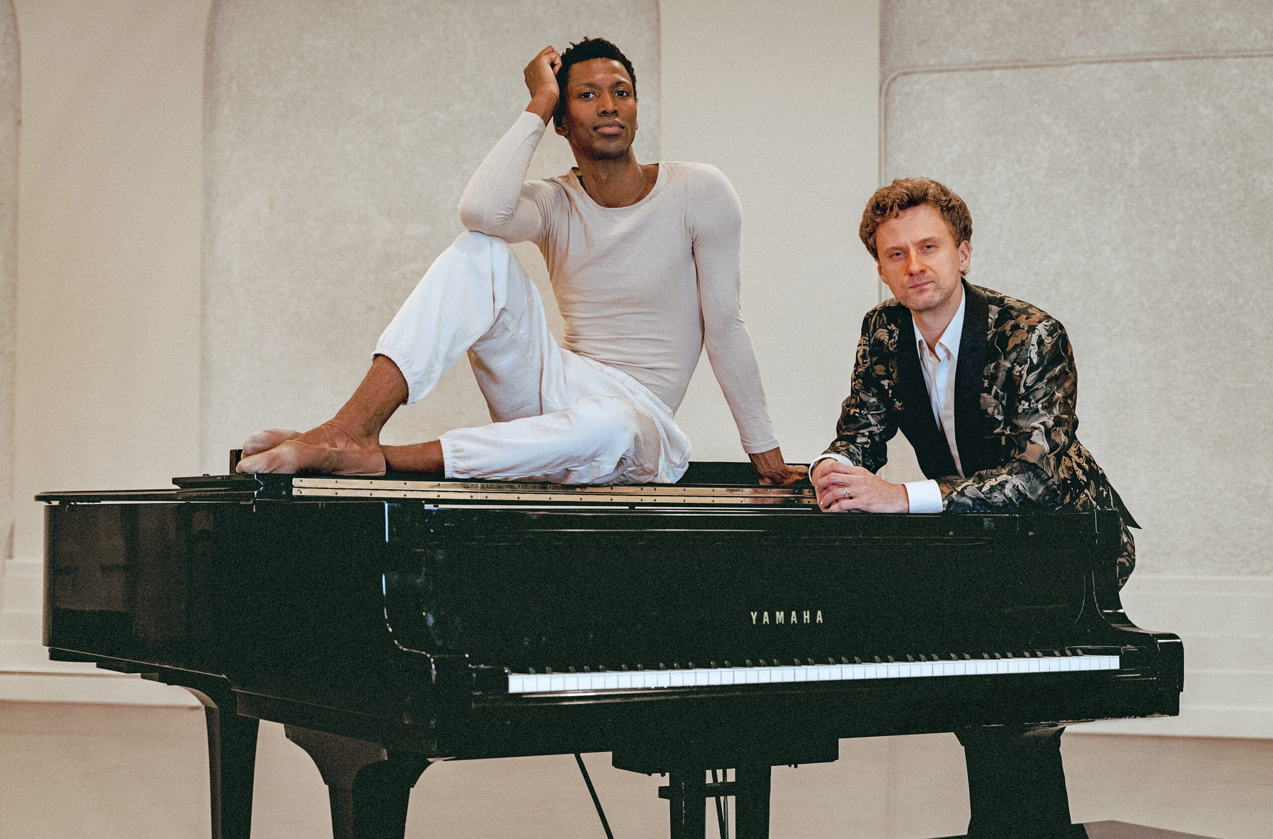 a male dancer sitting on top a grand piano with another man standing behind it