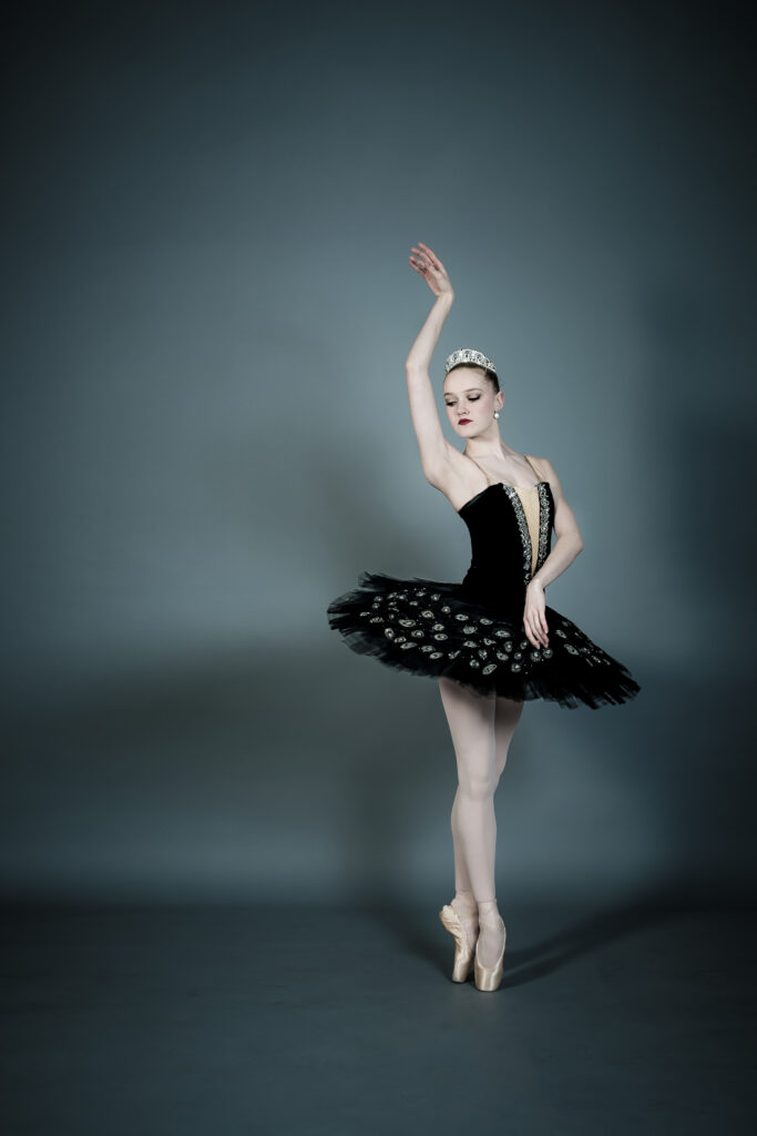 Sarah Lapointe poses in a black classical tutu. She is in sous-sus en pointe, one arm raised beside her head in a manner evocative of Swan Lake.