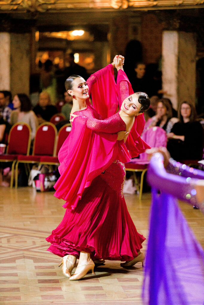 two female ballroom dancers wearing bright pink dresses dancing together at competition 