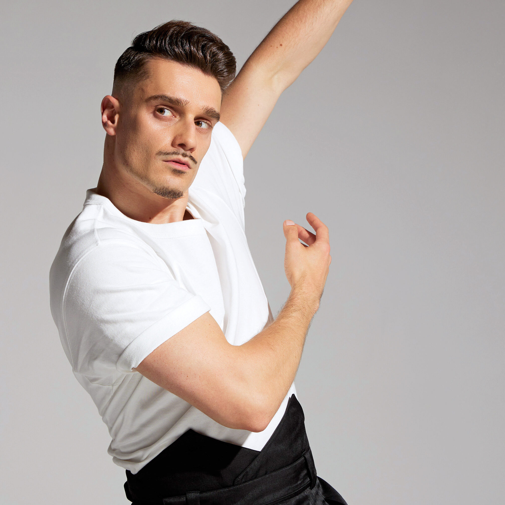 a male dancer in a white shirt and black pants with his arms swaying right 
