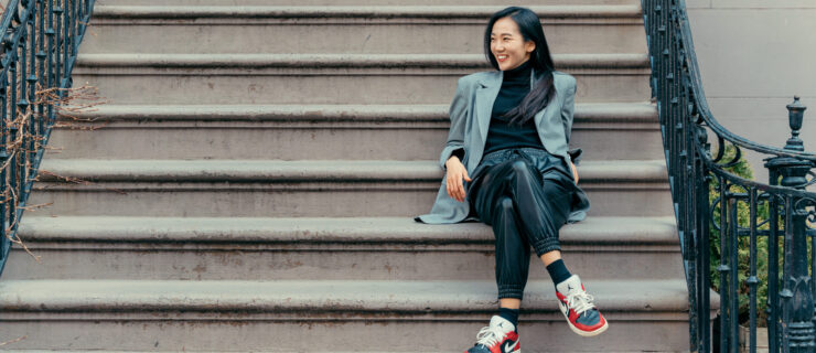 a female sitting on the steps wearing Nike sneakers, leather pants, and a green blazer