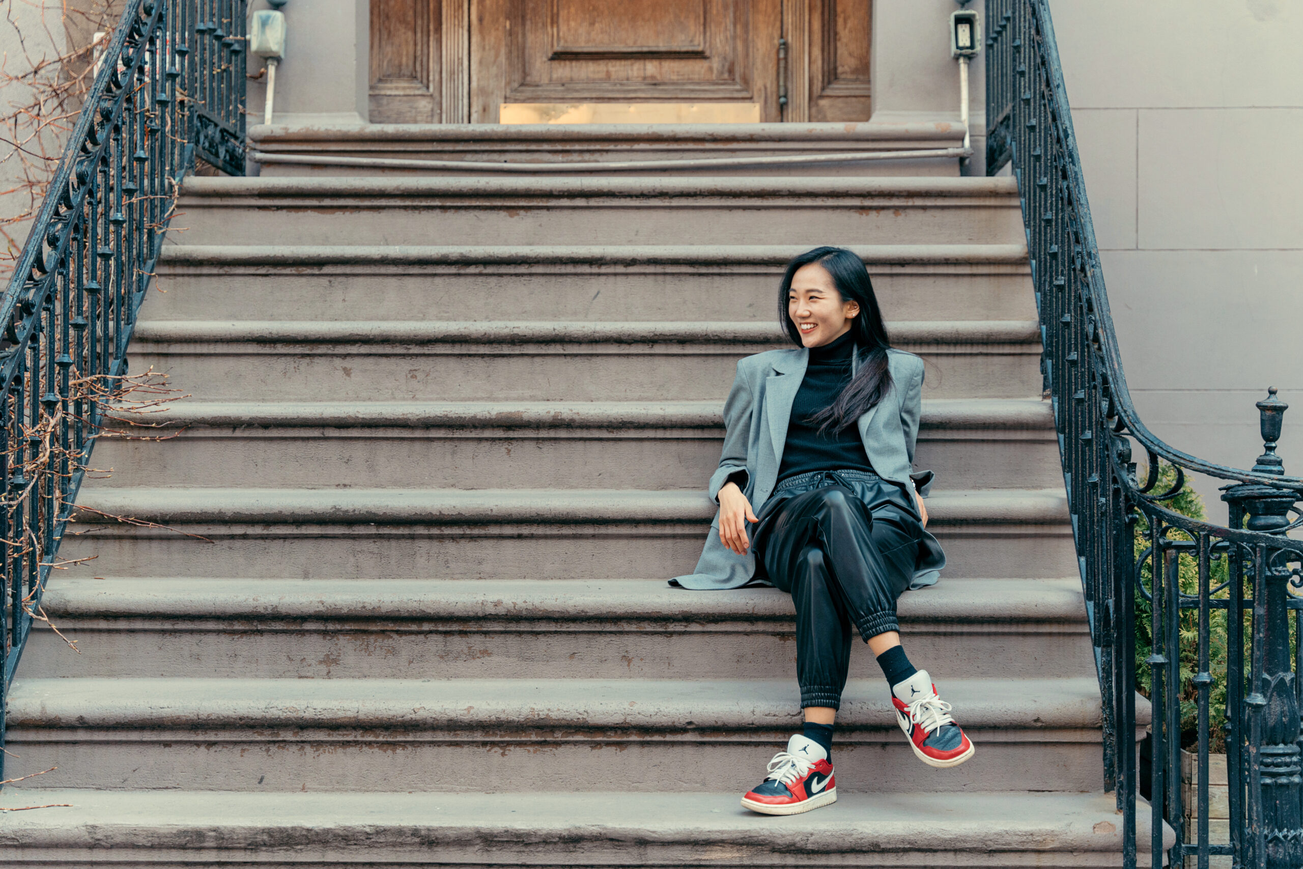a female sitting on the steps wearing Nike sneakers, leather pants, and a green blazer
