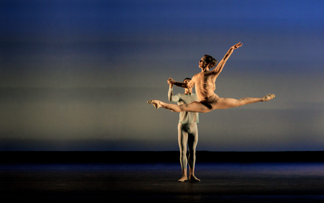 a male dancer supporting a female dancer as she grand jetes across the stage