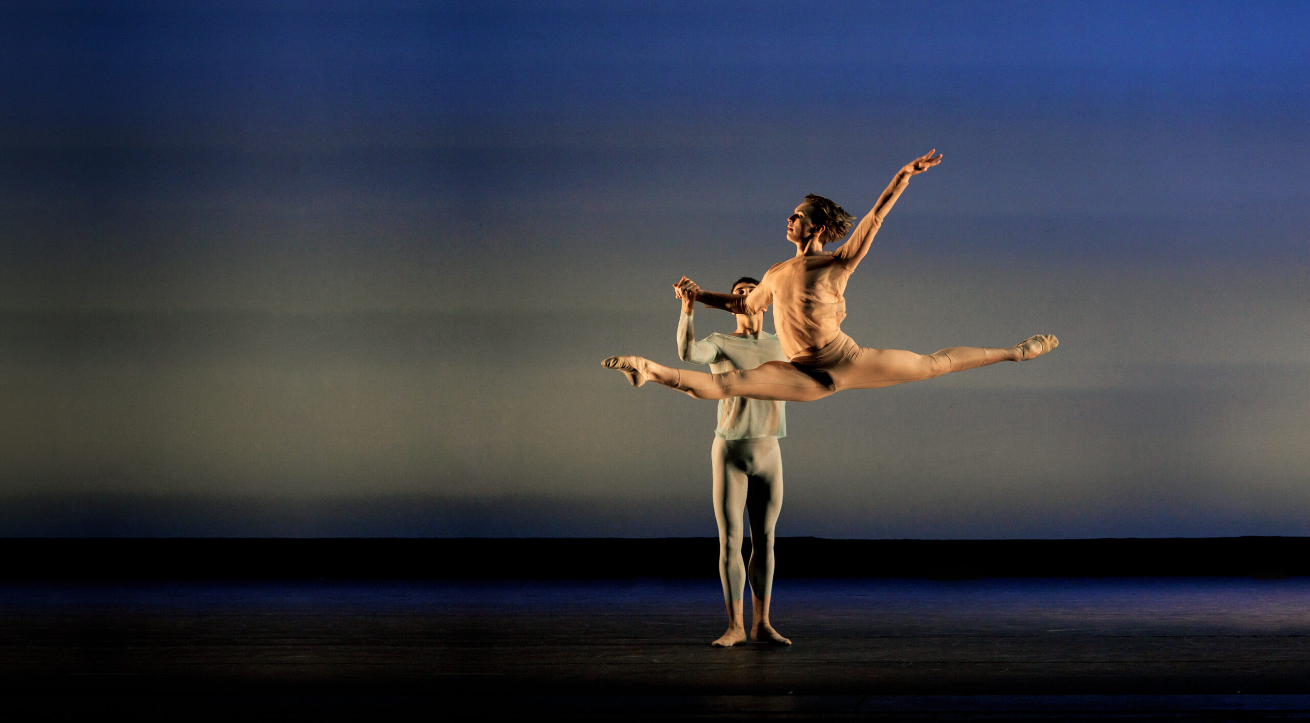 a male dancer supporting a female dancer as she grand jetes across the stage