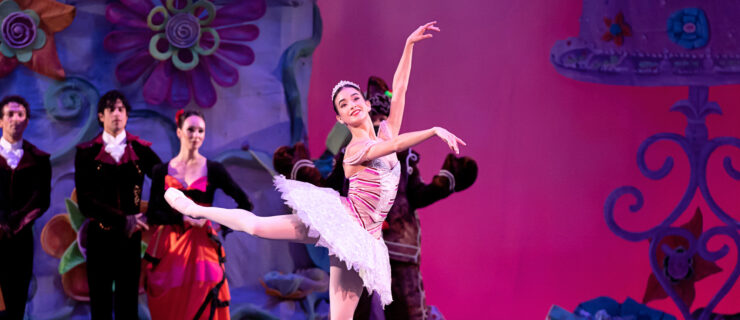 a female ballerina performing an attitude derriere arms in 3rd while wearing a purple tutu and tiara
