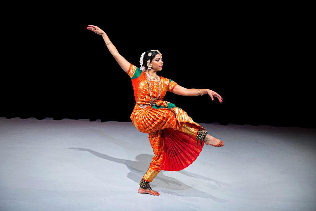 a female dancer wearing a traditional long dress extending on leg front in attitude with arms at a diagonal 