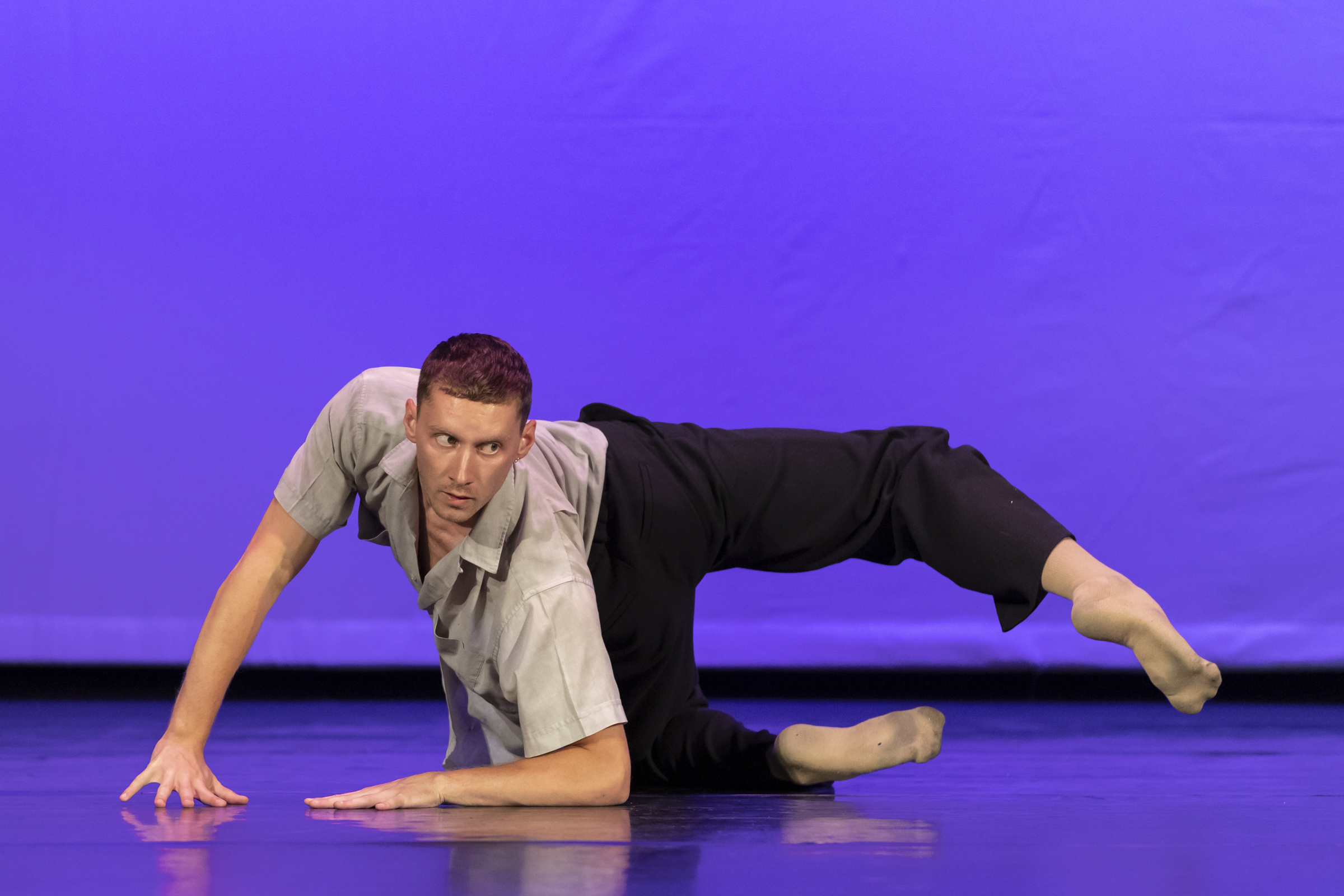 During a solo onstage, Andrew McShea contorts his body to look toward the audience while his hips and legs face backward. He holds himself up on the floor with his arms and lifts his top leg in a bent shape.