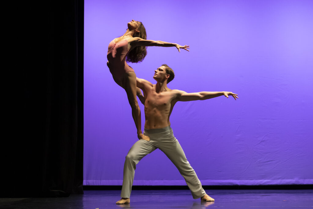 Cameron Catazaro and Ashley Knox perform "After the Rain" onstage. Catazaro stands in a deep lunge and supports Knox with his right arm; Knox stands on Catazaro's front quad and arches backward in a low arabesque, head and chest turned upward and arms extended behind her.