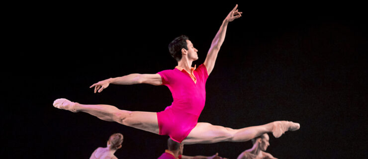 a male dancer wearing a pink unitard performing a grand jete on stage