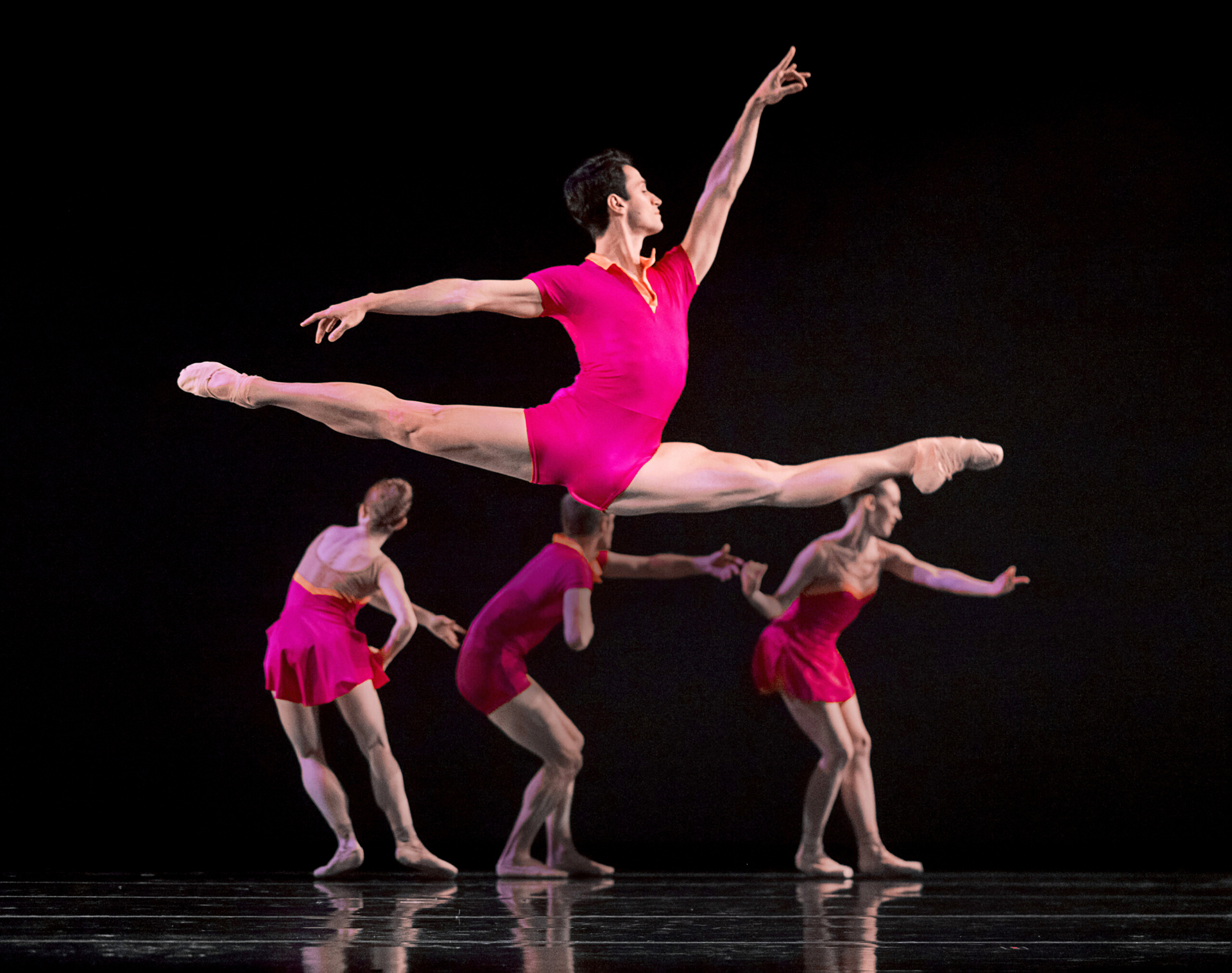 a male dancer wearing a pink unitard performing a grand jete on stage