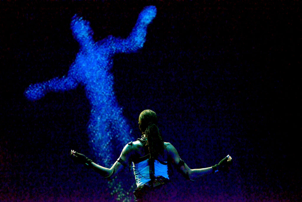 a dancer with her back to the camera looking up at an AI projection 