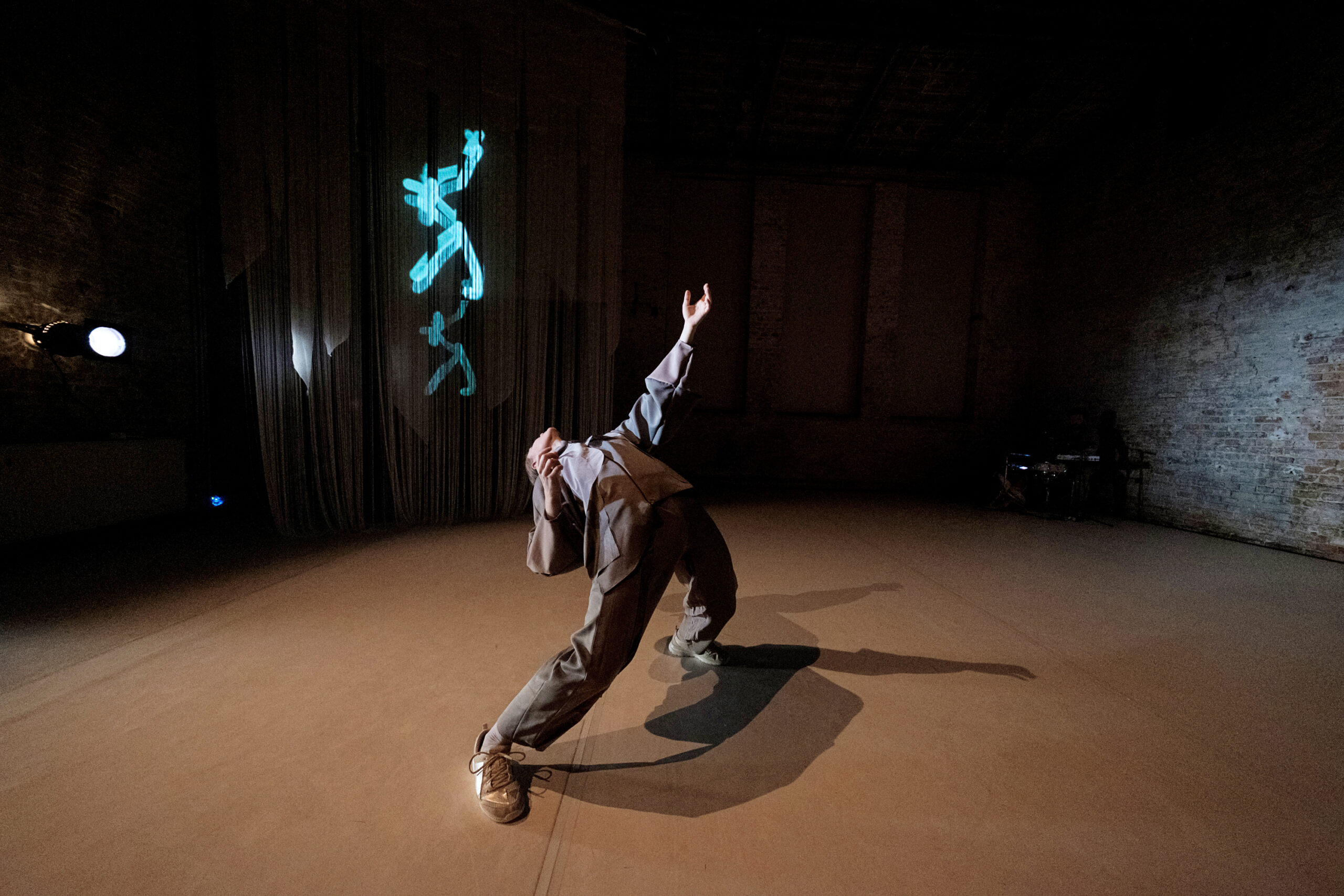 a male dancer leaning back and reach up with a projection displayed on the curtain behind him
