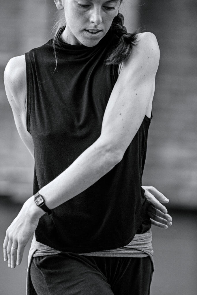 a female dancer wearing a black tank top with arms twisting around her torso 