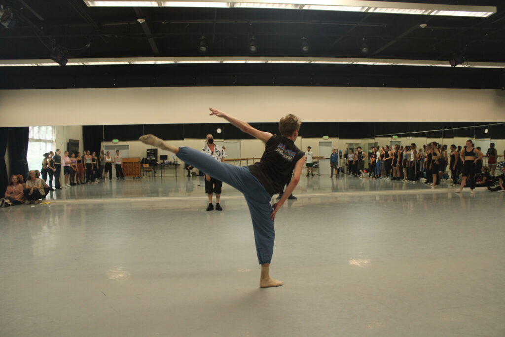 a male dancer in the center of the studio performing an arabesque 