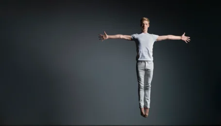 a male dancer jumping straight up with his arms extended directly out