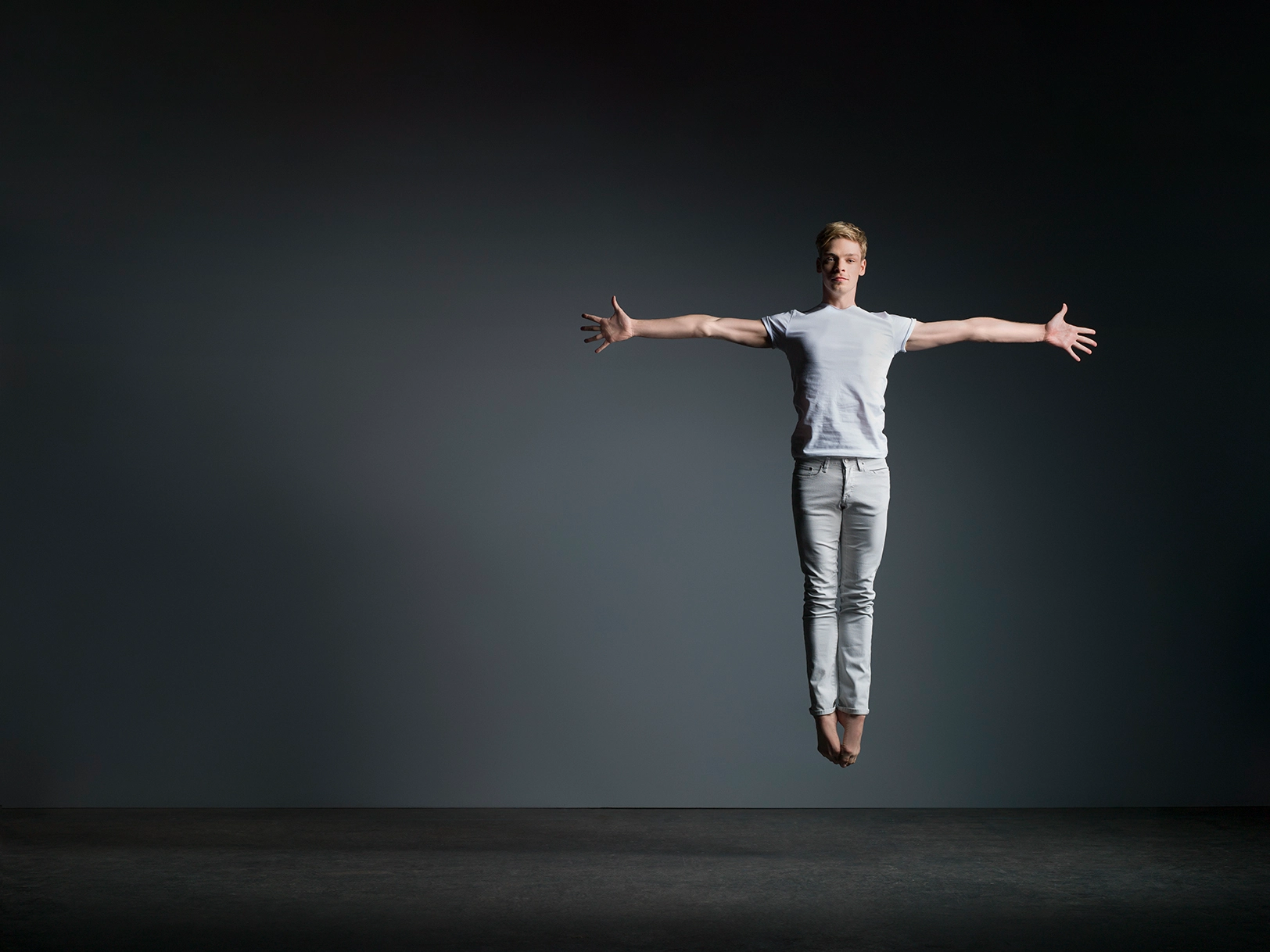 a male dancer jumping straight up with his arms extended directly out