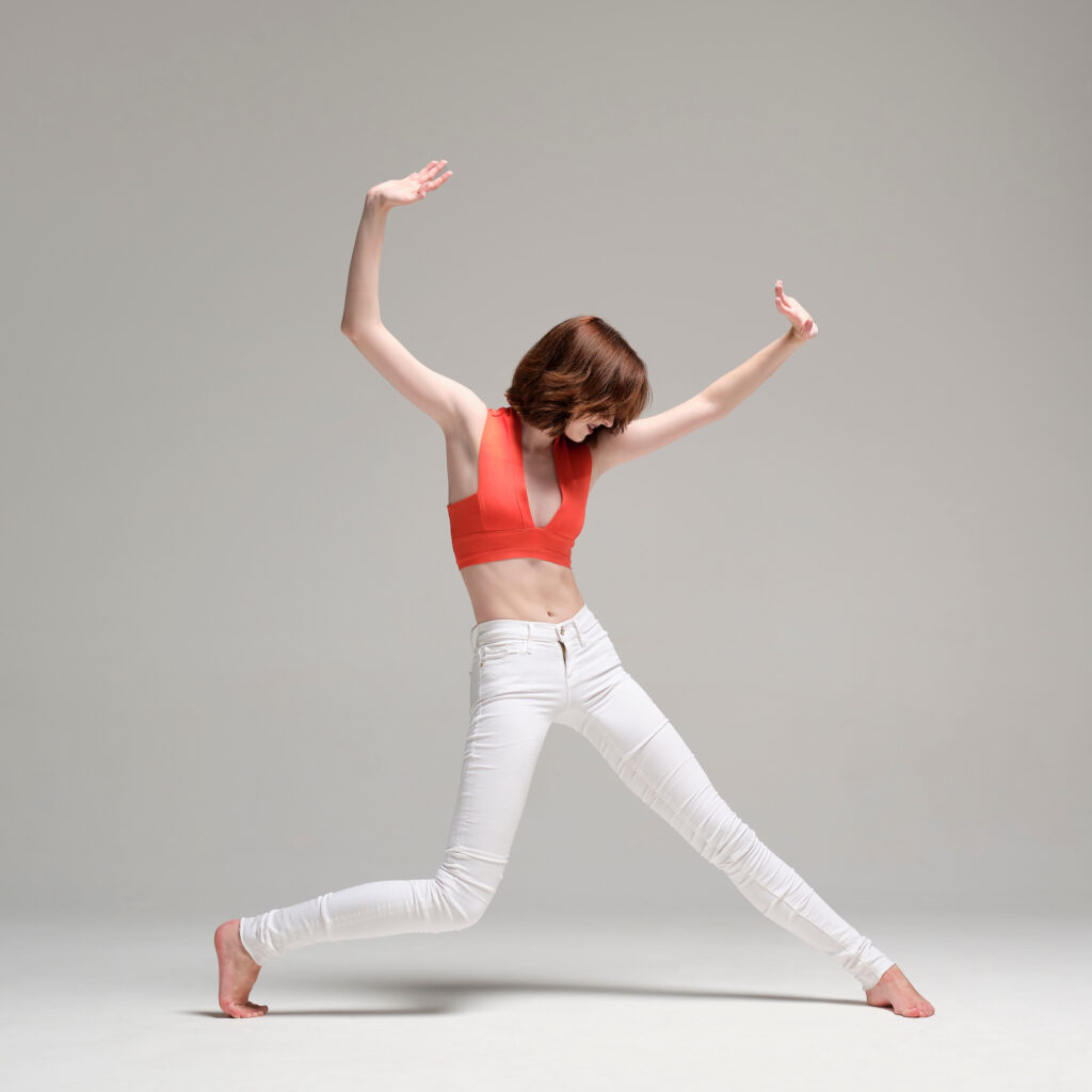 a female dancer wearing white jeans and red top lunging and reaching up