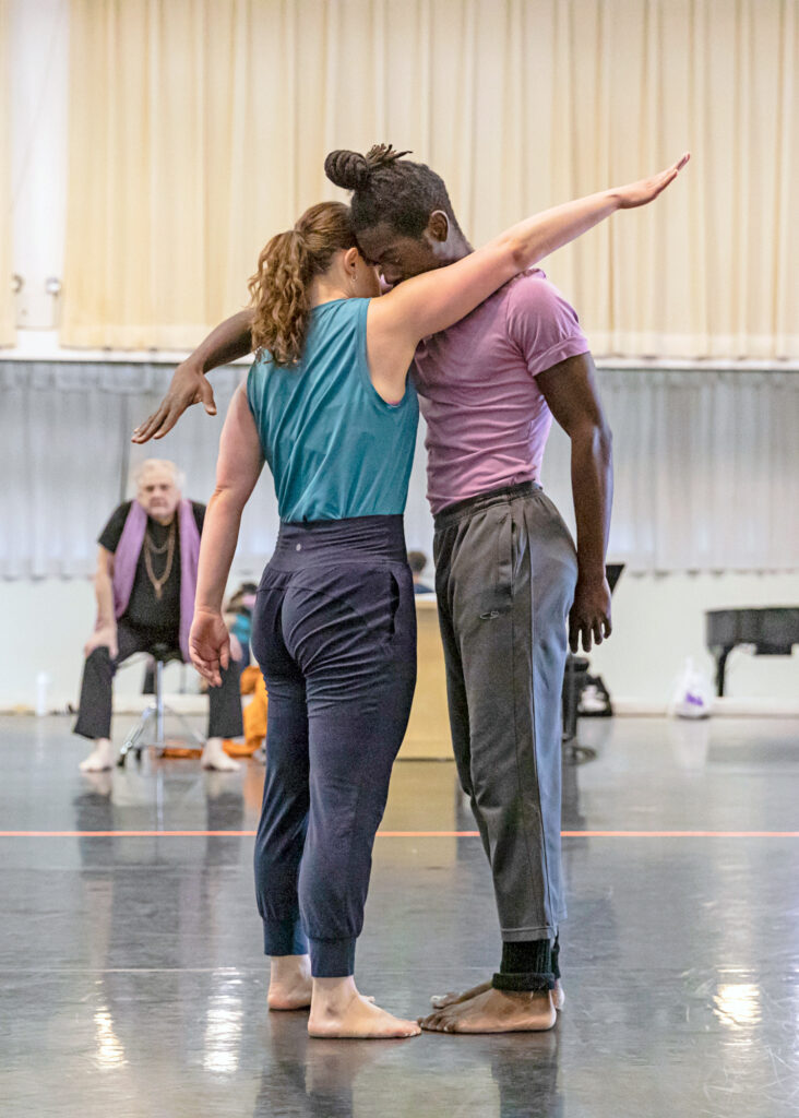 two dancers standing face to face with one arm reaching past their partner