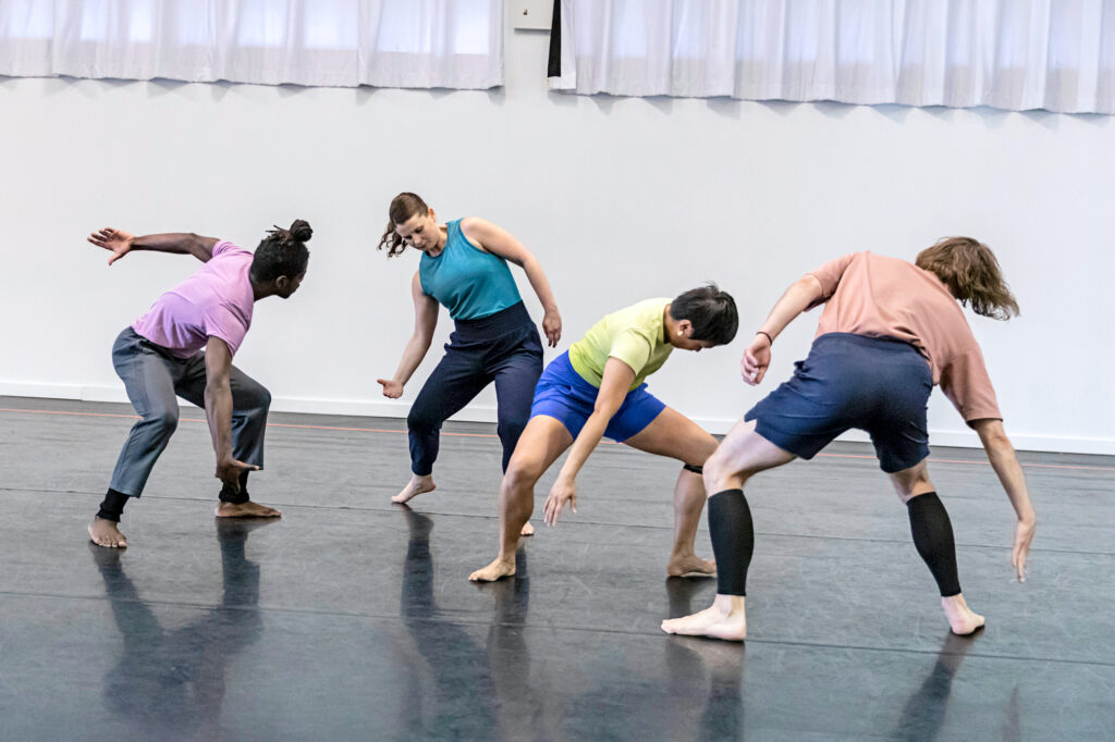 a group of 4 dancers in rehearsal falling to the side