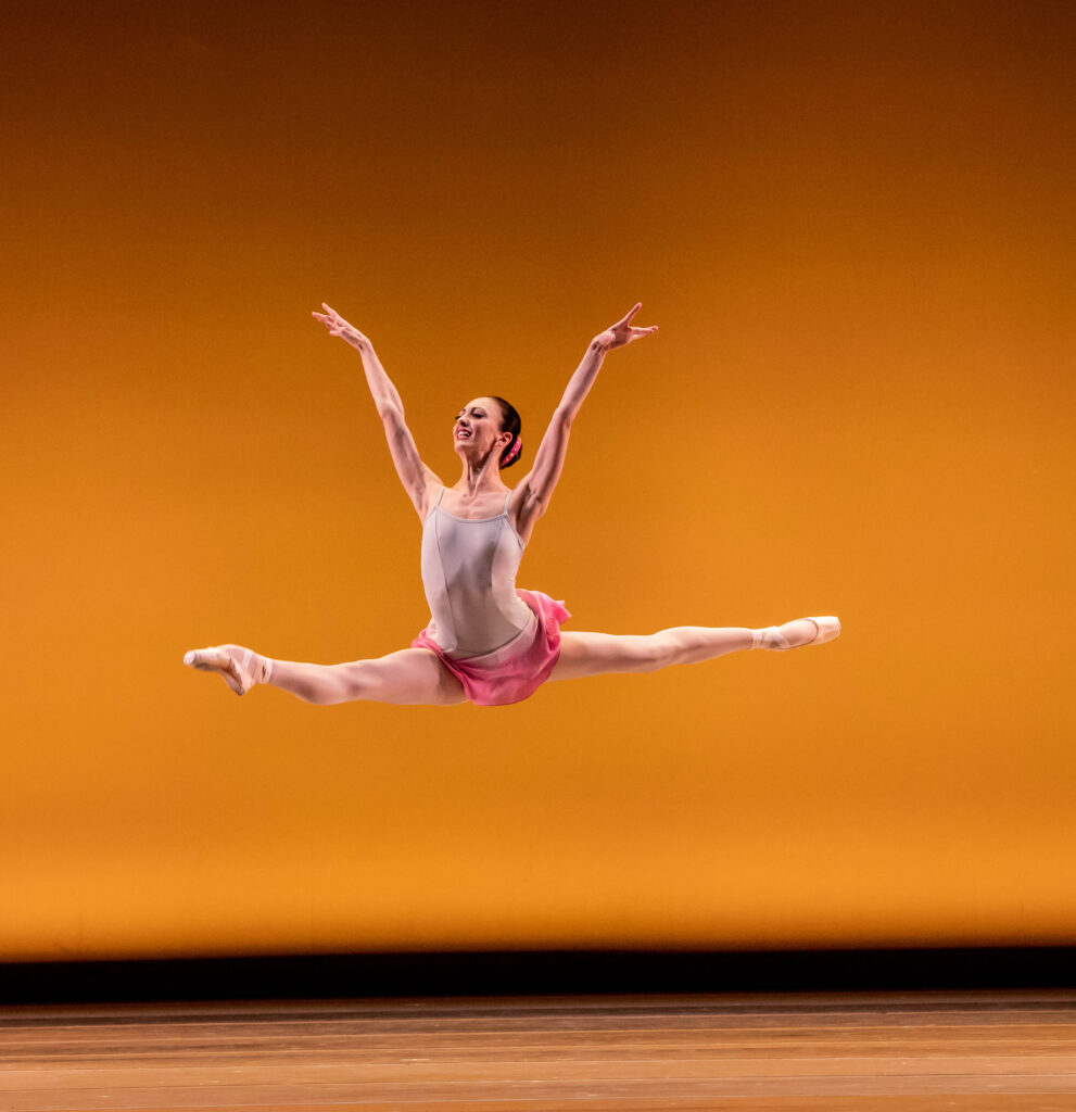 a female dancers performing a grand jete on stage