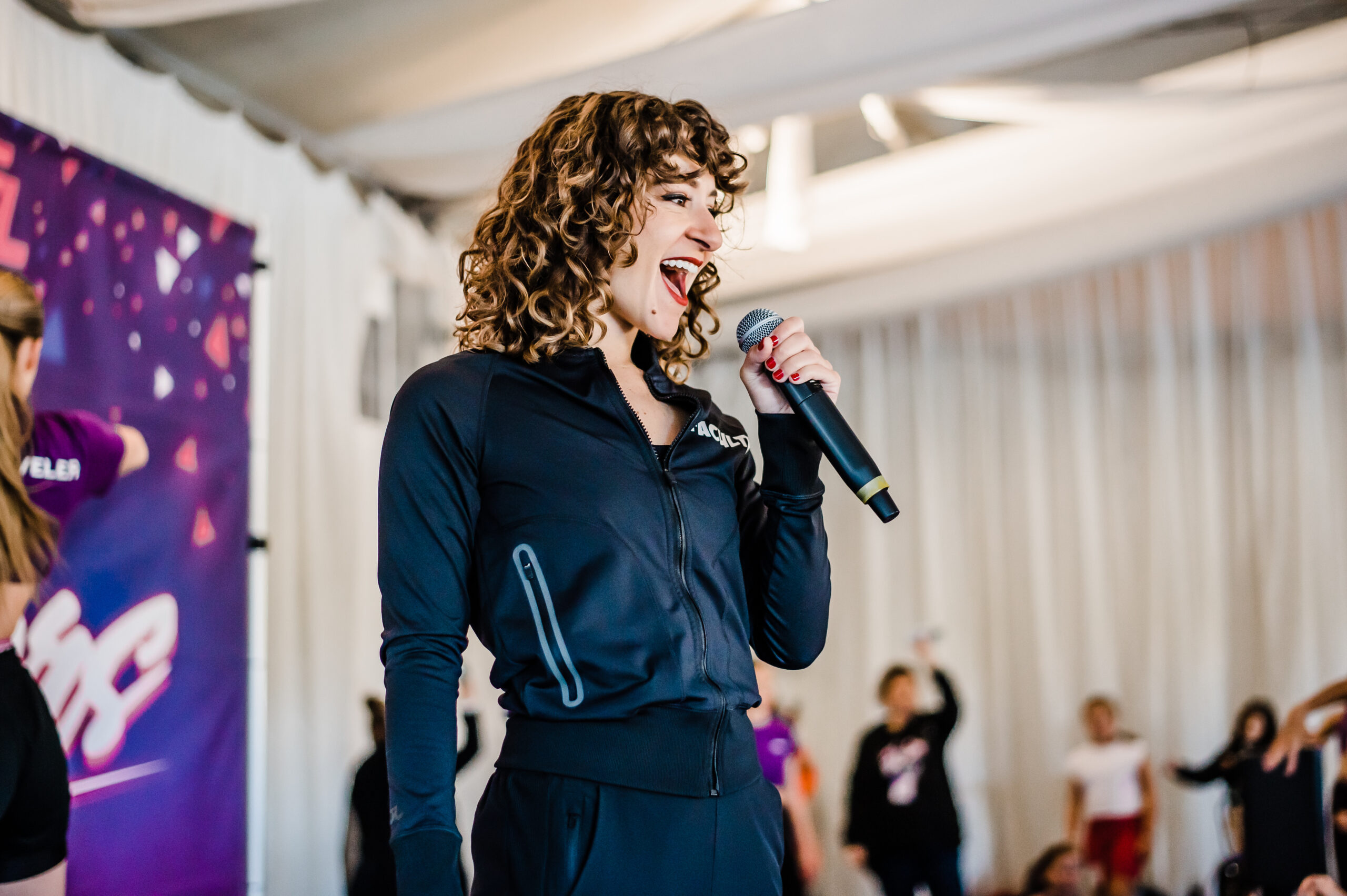 a female wearing black with curly hair speaking into a microphone